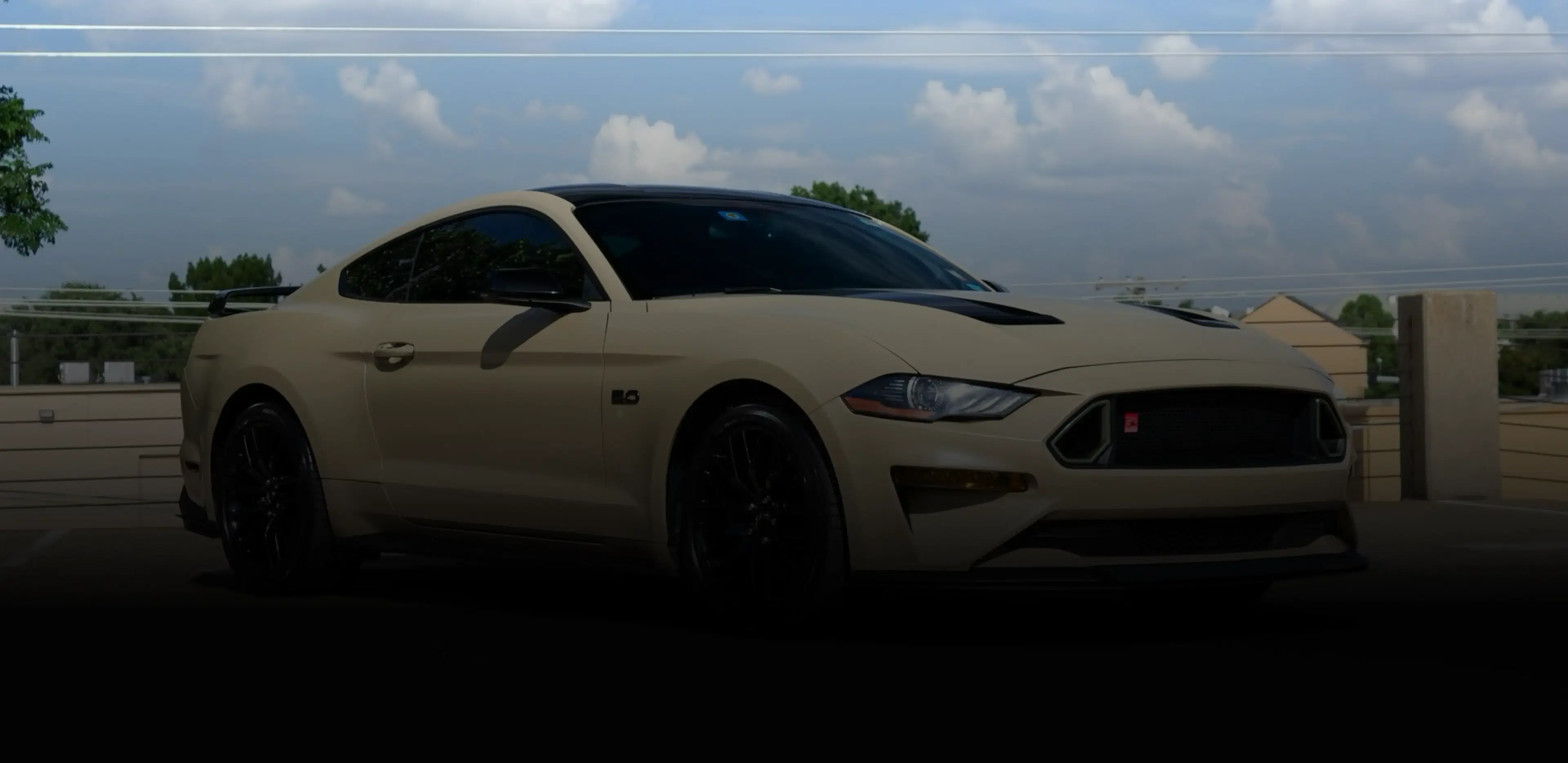 Beige Mustang parked in front of a fence, showcasing Speed Shield USA's automotive PPF, vinyl wrap, and window tint services.